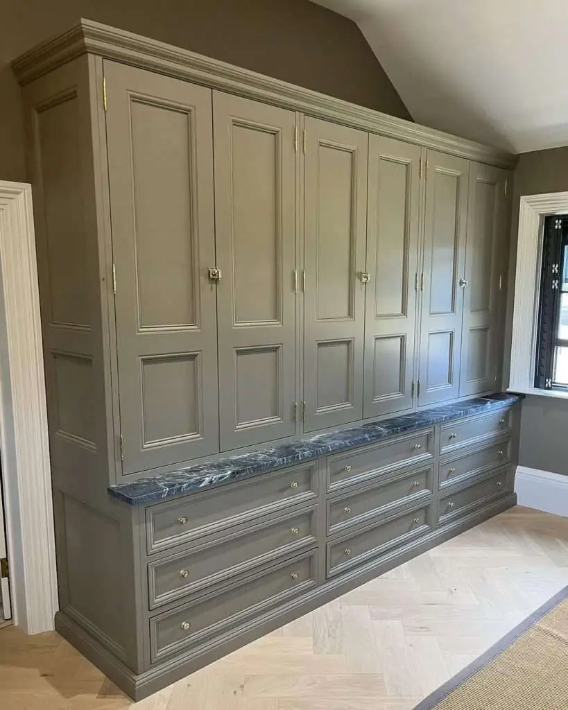 Painted fitted wardrobe with panelled doors and drawers beneath a sloping ceiling