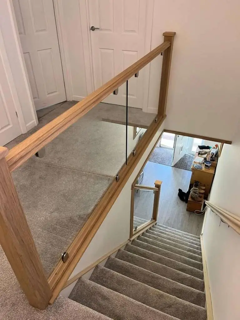 Oak handrail and clear glass guarding above a carpeted staircase