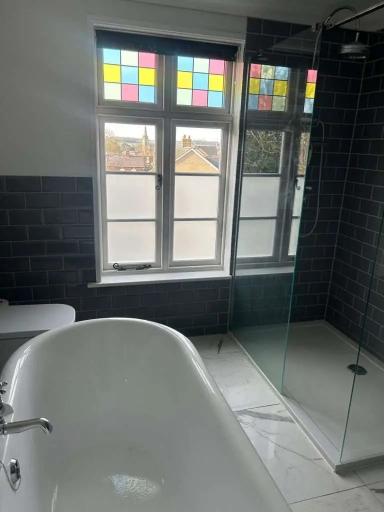 White timber window and decorative coloured glazing above a freestanding bath