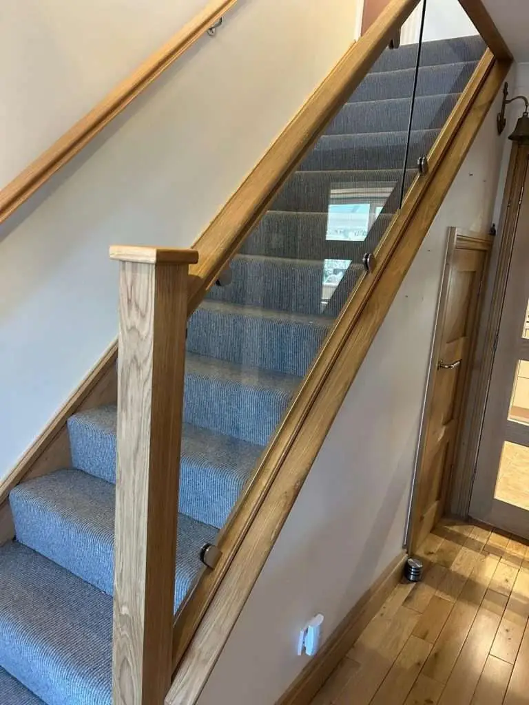 Carpeted staircase with oak handrails and clear glass panels
