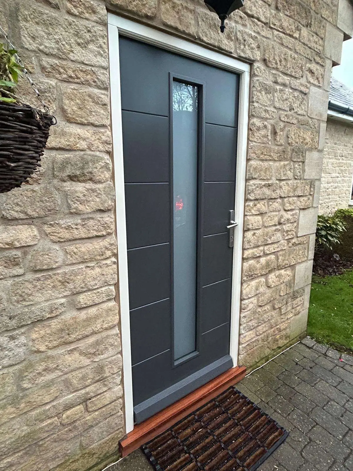 Grey panelled entrance door with a narrow glazed panel in a stone wall