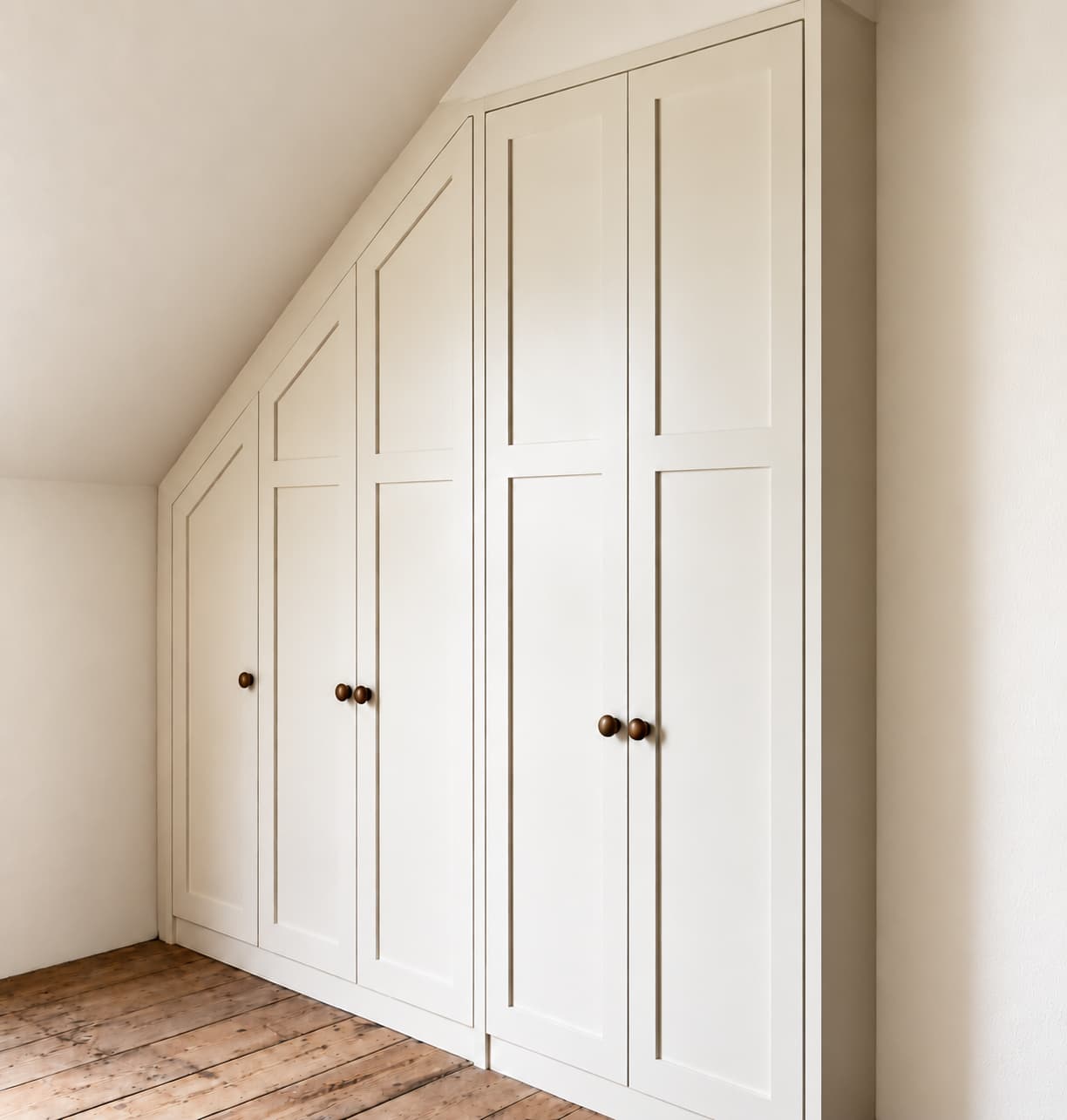 White panelled fitted wardrobes following a sloping bedroom ceiling